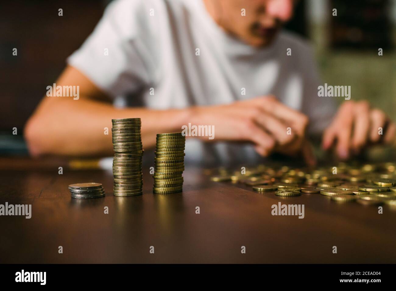 anonimo giovane uomo contando le monete lucenti e impilandole sopra tavolo di legno Foto Stock