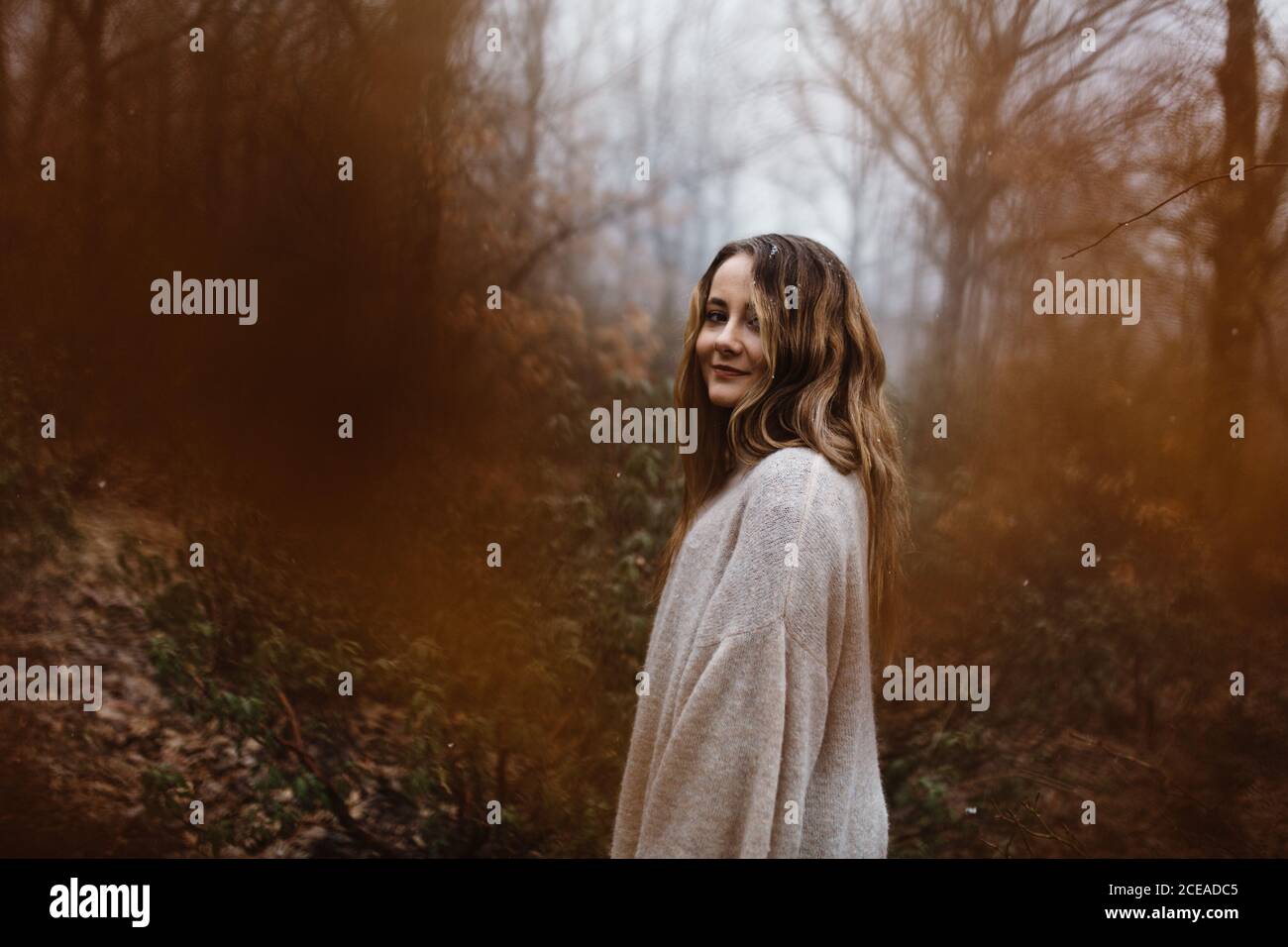 Vista laterale di una donna sorridente attraente in piedi nella foresta autunnale. Foto Stock
