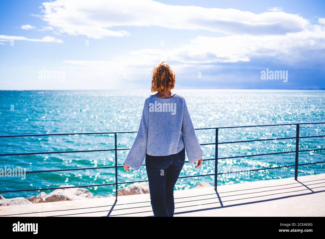 Donna in piedi al corrimano e guardando l'oceano Foto Stock