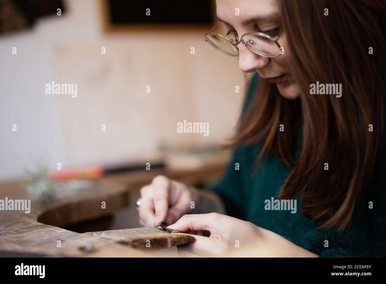 Ritaglia le mani ravvicinate della donna intagliando e spazzolando piccoli dettagli con il pennello alla scrivania Foto Stock