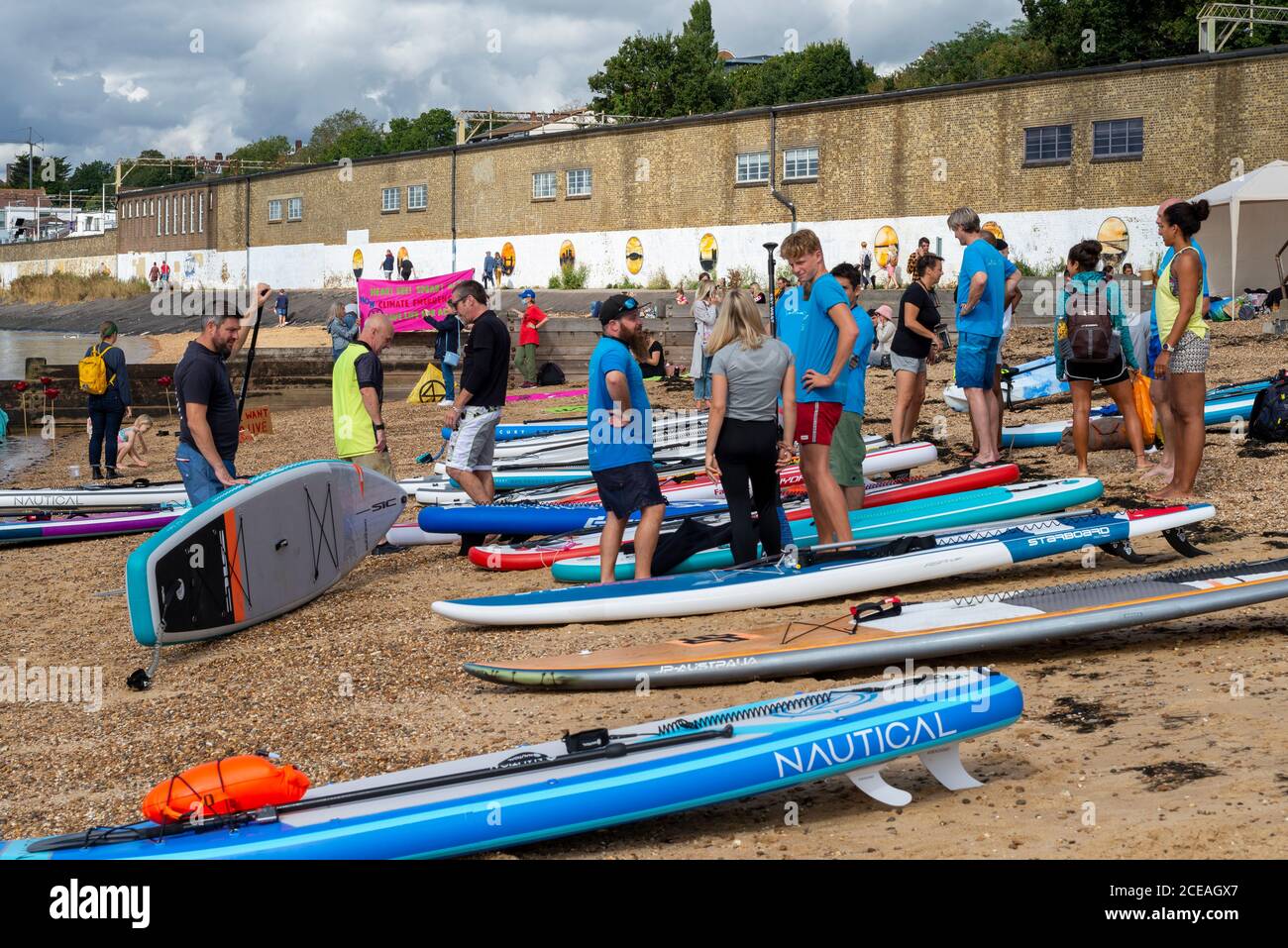 Un grande gruppo di stand up paddle boarder che si preparano a prendere le loro tavole fuori sull'estuario del Tamigi a Chalkwell Beach, Southend on Sea, Essex, Regno Unito Foto Stock