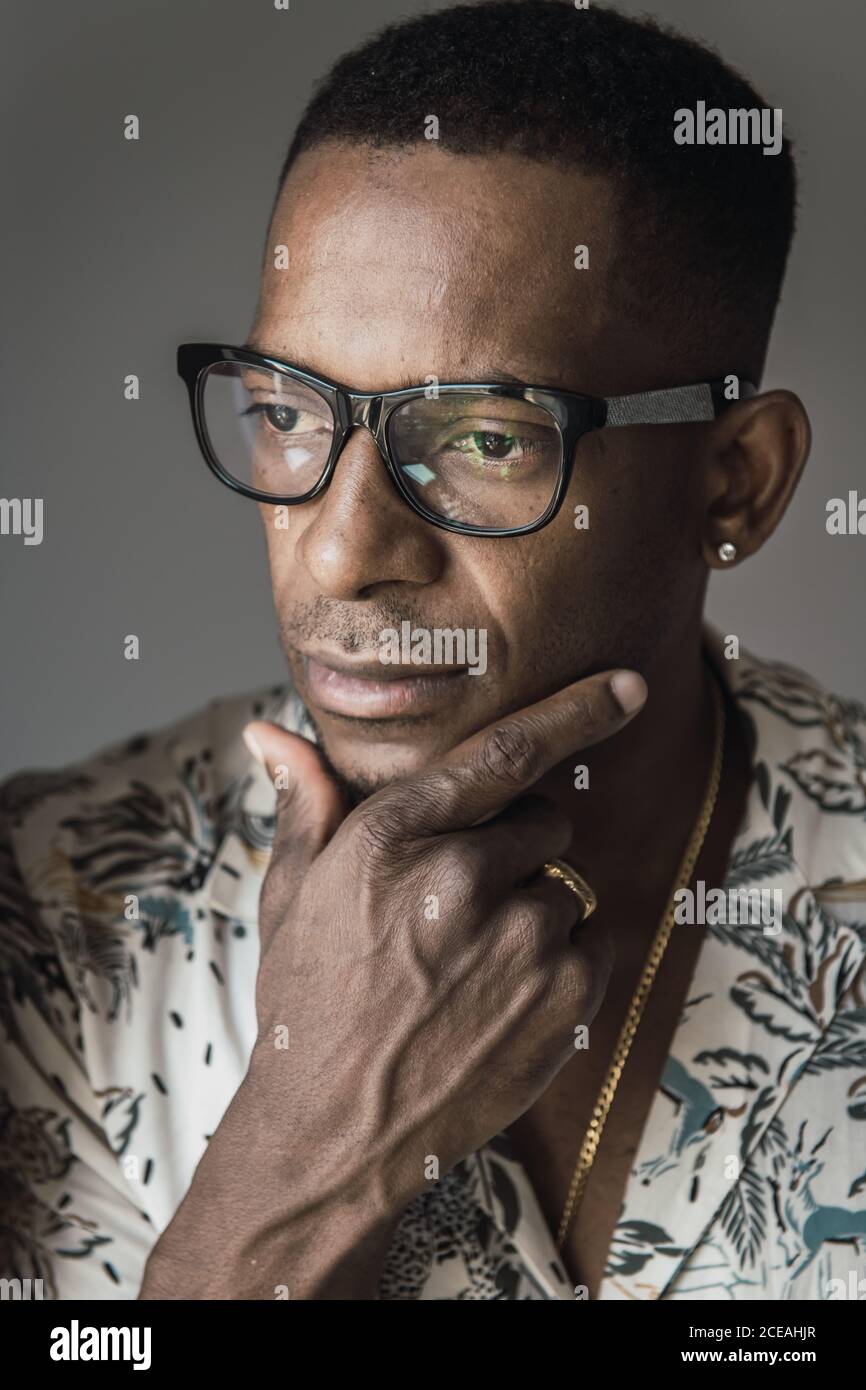 Colpo di testa di un serio uomo afroamericano adulto in oro accessori e occhiali che toccano il mento Foto Stock