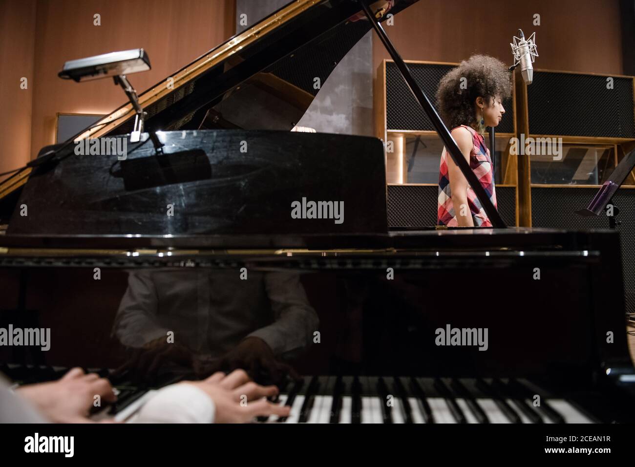 Crop uomo che suona piano mentre provando in studio di registrazione con cantante femminile. Foto Stock