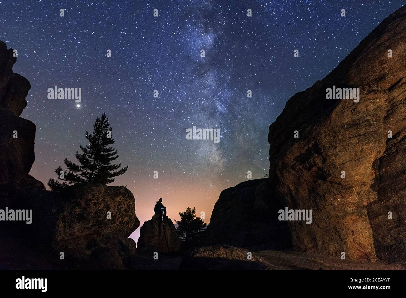Uomo seduto sotto le stelle Via Lattea nella roccia silhouette montagne. Soria, Spagna Foto Stock