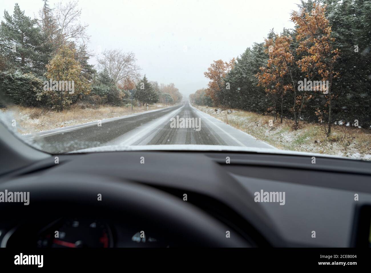 Guidare una macchina su una strada innevata durante una nuvolosa giorno invernale Foto Stock