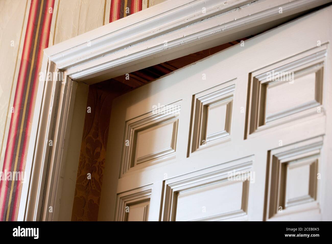 Dal basso si può ammirare l'angolo della porta bianca socchiusa in camera con carta da parati a righe Foto Stock