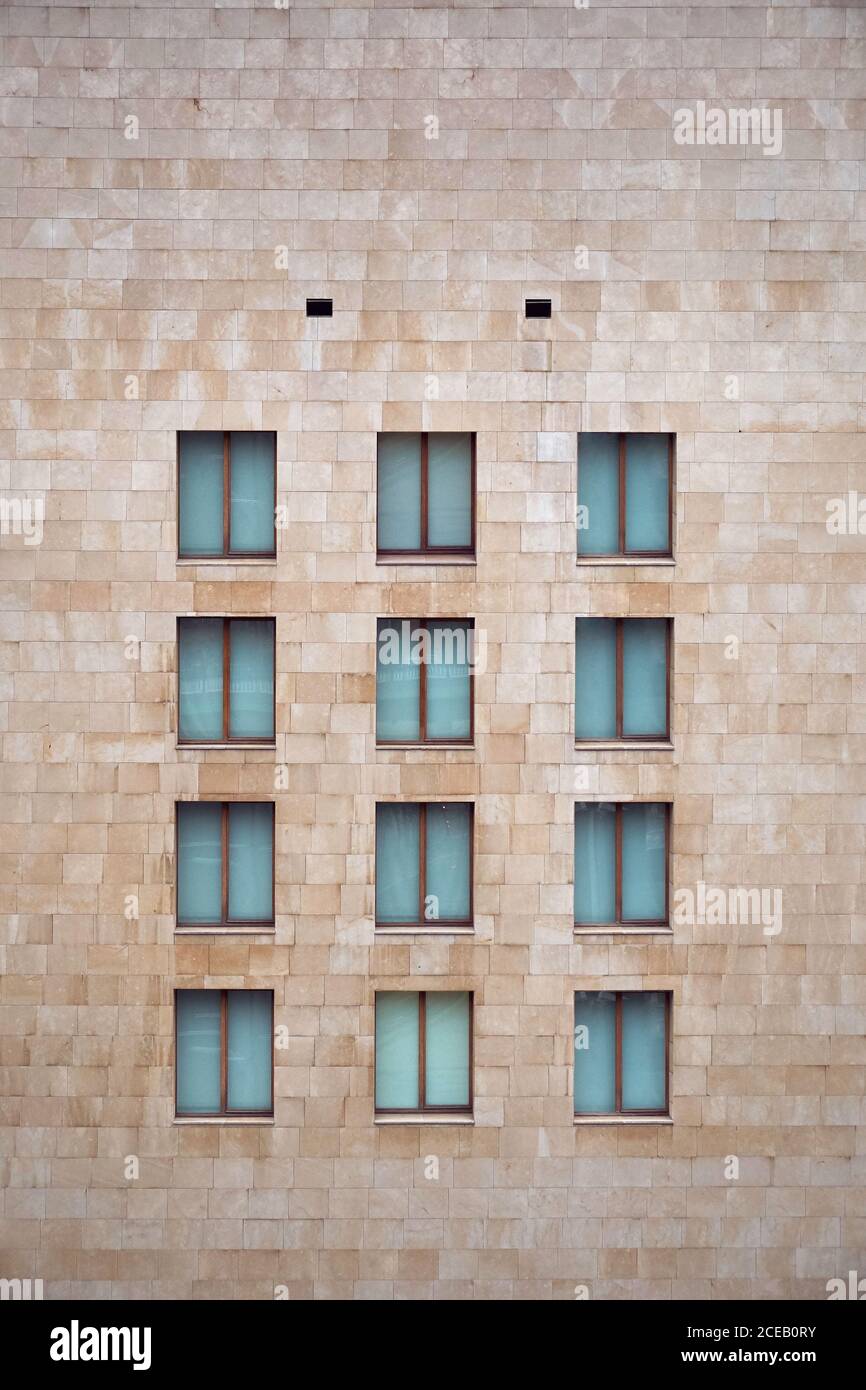Parete di mattoni marrone chiaro dell'edificio con piccole finestre chiuse simili A Bilbao Foto Stock