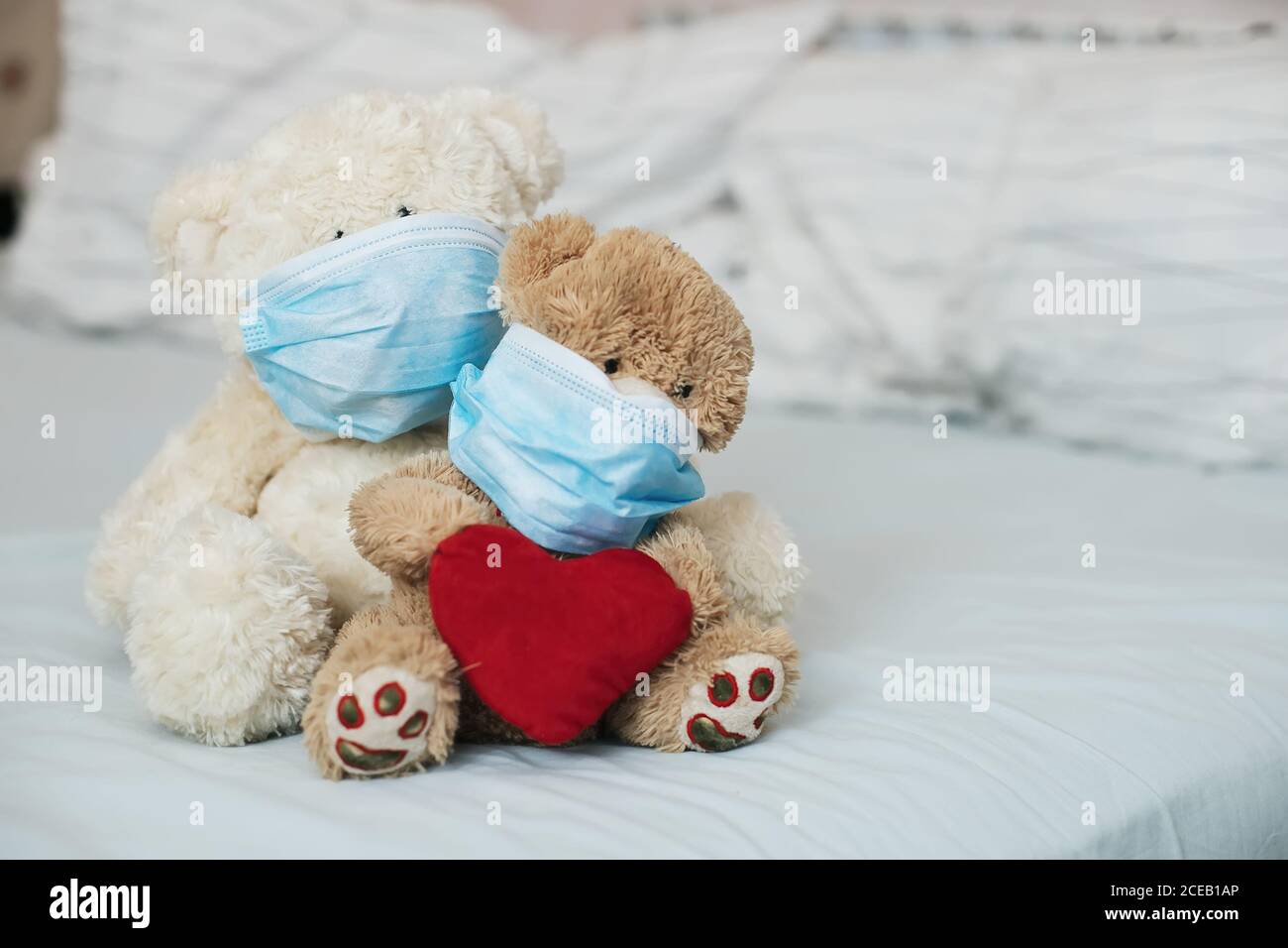 Due orsi giocattolo con cuore rosso con maschere mediche di protezione sul letto. Malattia falciforme nei bambini. Coronovirus, quarantena, epidemia, pandemia, freddo, illne Foto Stock