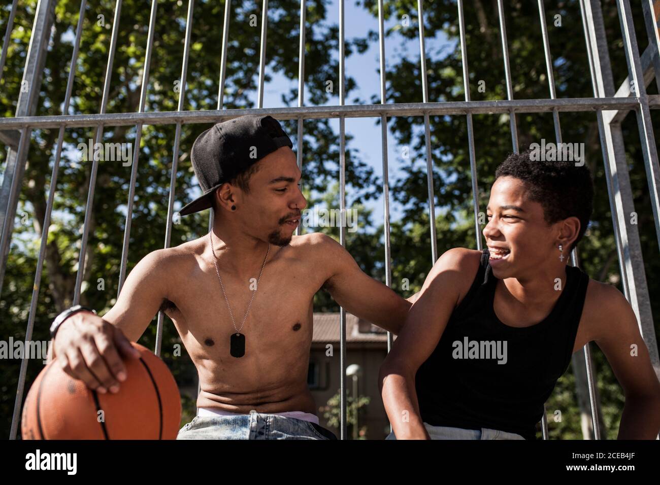 I giovani fratelli afro giocano a basket sul campo della loro quartiere sorridente e abbracciante Foto Stock