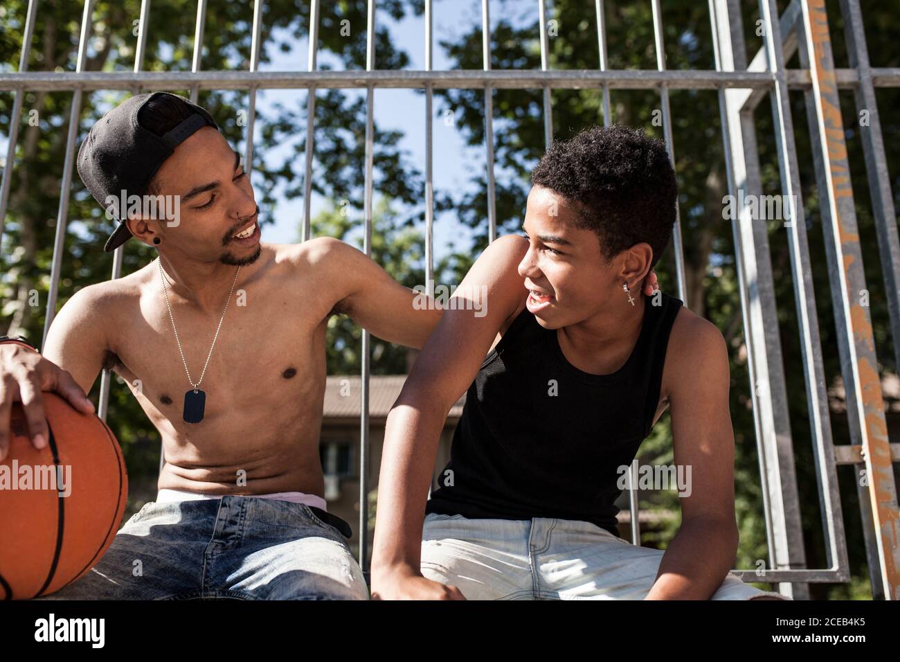 I giovani fratelli afro giocano a basket sul campo della loro quartiere sorridente e abbracciante Foto Stock