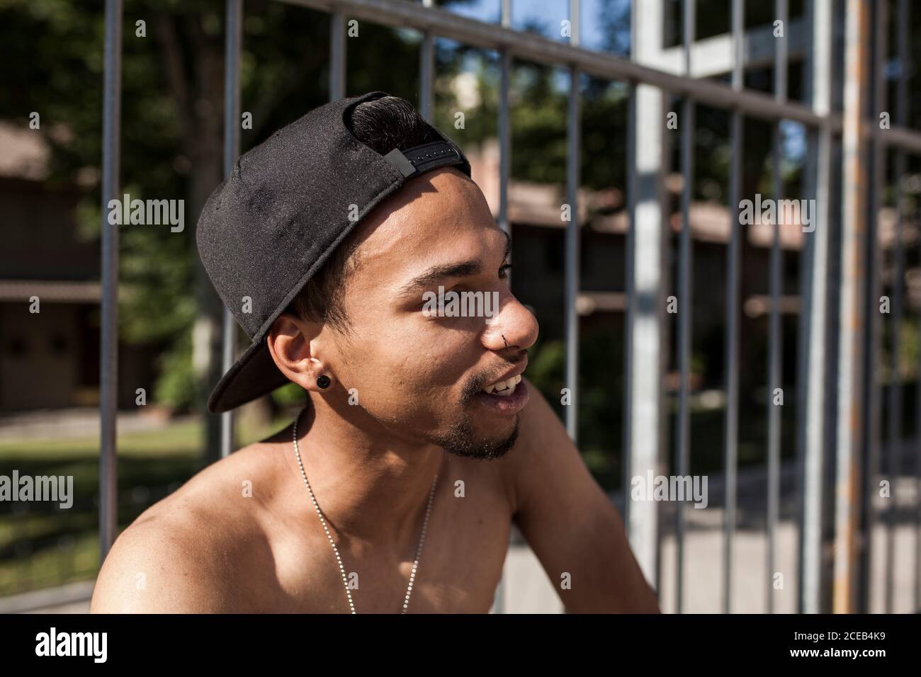 afro giovane ragazzo con cappello gioca a basket sul campo del suo quartiere sorridendo, ritratto guarda a destra Foto Stock
