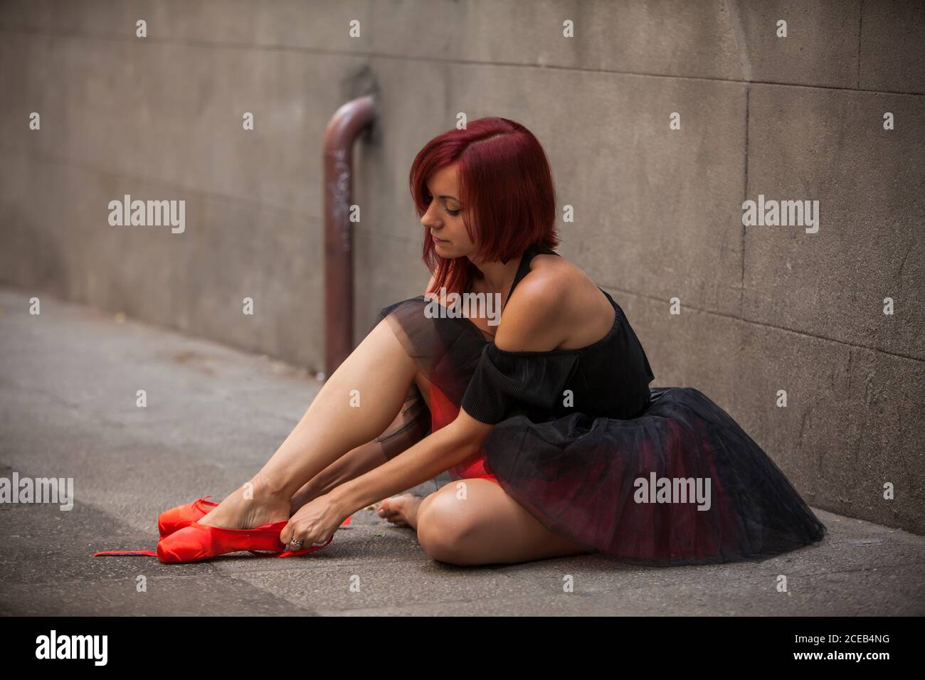 Testa ballerina rossa con tutu nero che batte le punte del balletto rosso sulla strada Foto Stock
