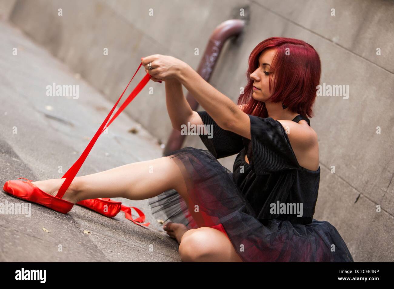 Testa ballerina rossa con tutu nero che batte le punte del balletto rosso sulla strada Foto Stock