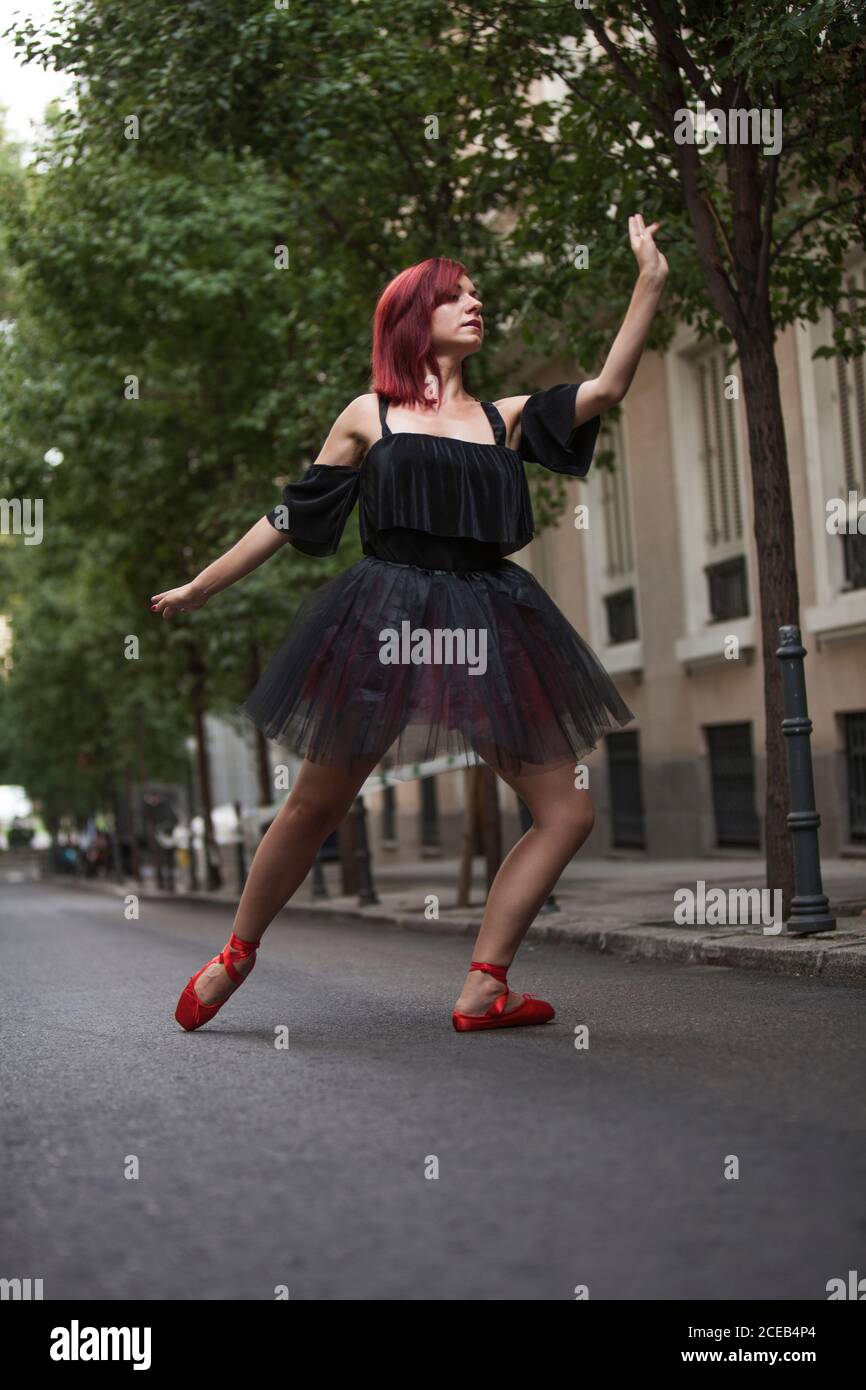 Testa ballerina rossa con tutu nero e balletto rosso che danzano sulla strada con alberi sullo sfondo. Foto Stock