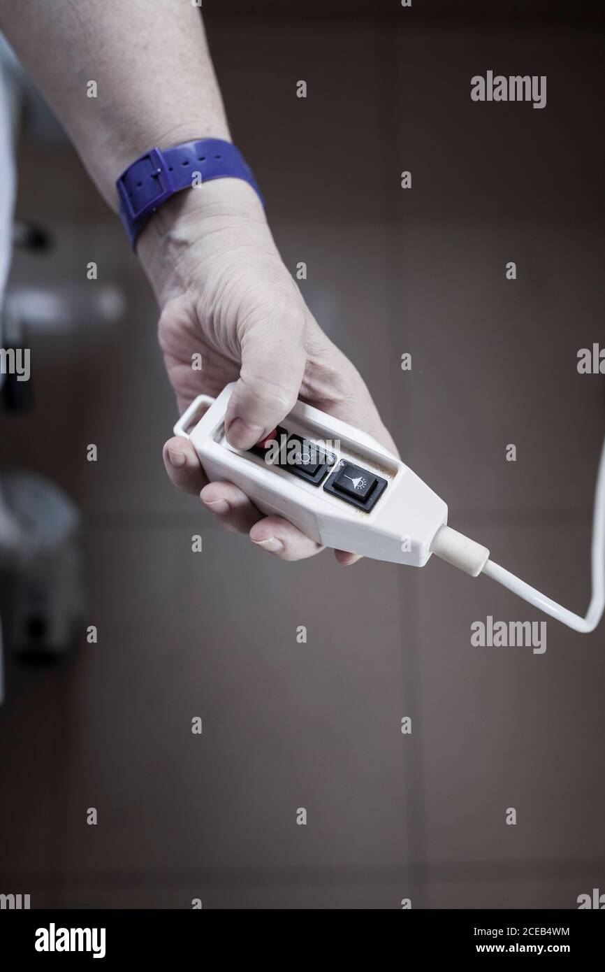 Donna matura irriconoscibile ricoverata in ospedale per la chirurgia del ginocchio, seduta sulla sedia e tenendo il controllo di chiamata Foto Stock