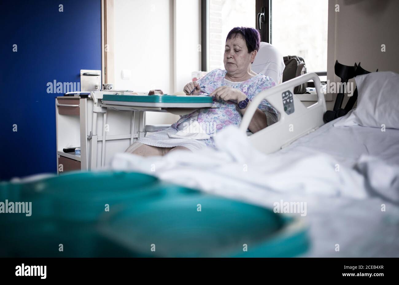 Donna matura irriconoscibile ricoverata in ospedale per la chirurgia del ginocchio, seduta sulla sedia, mangiare cibo dal vassoio Foto Stock