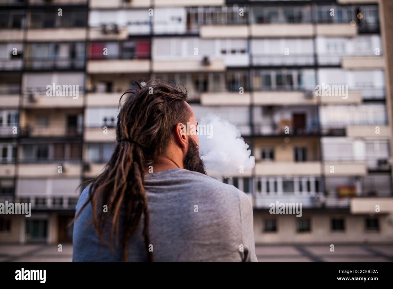 Giovane e caucasico uomo Rastafariano fumare ed esporre il fumo da dietro e guardare a destra Foto Stock