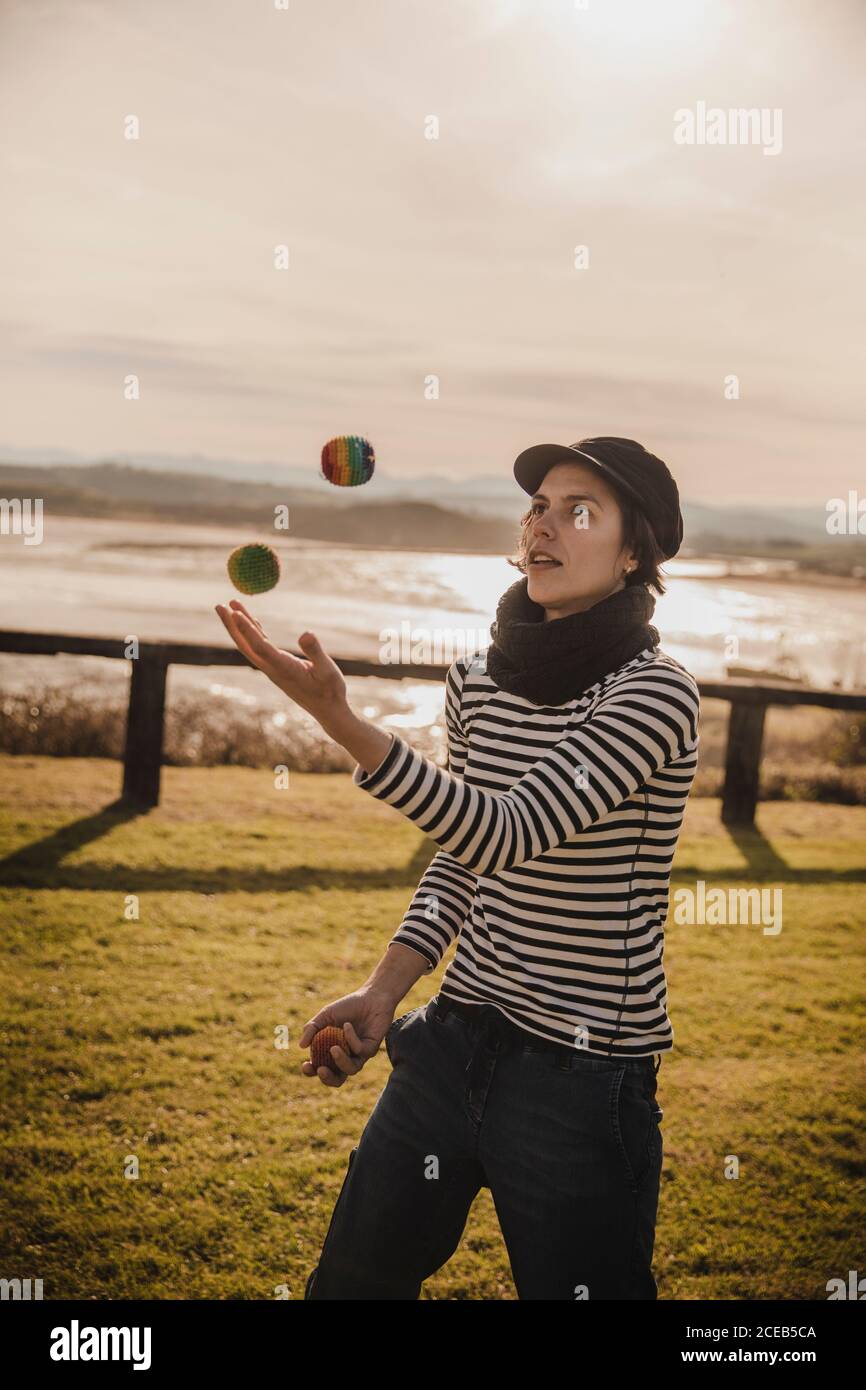 Elegante signora nel cappuccio juggling balls sull'erba vicino alla costa del mare e del cielo con Sun Foto Stock