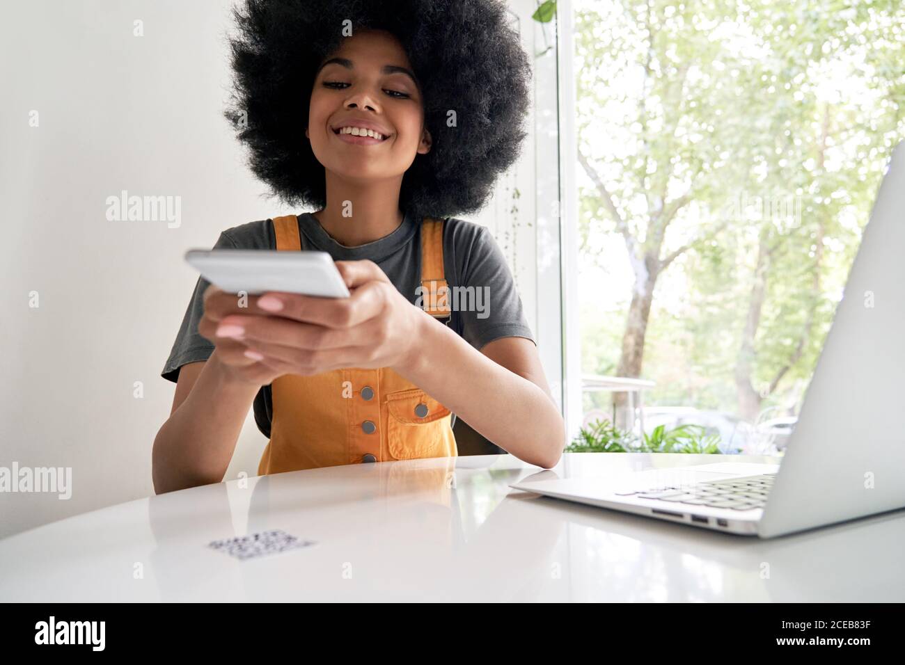 Sorridente donna africana che tiene smartphone scansione QR-code sul tavolo da caffè. Foto Stock