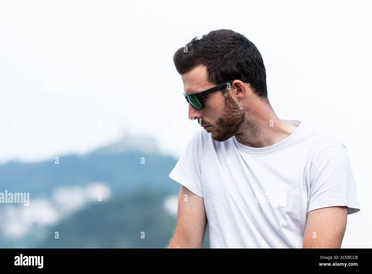 Giovane pensieroso in occhiali da sole e t-shirt bianca in piedi e. guardando via Foto Stock