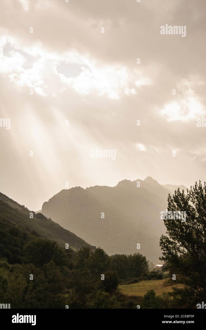 Fasci di sole luminoso che brillano attraverso le nubi spesse sopra stupefacente montagne una valle Foto Stock