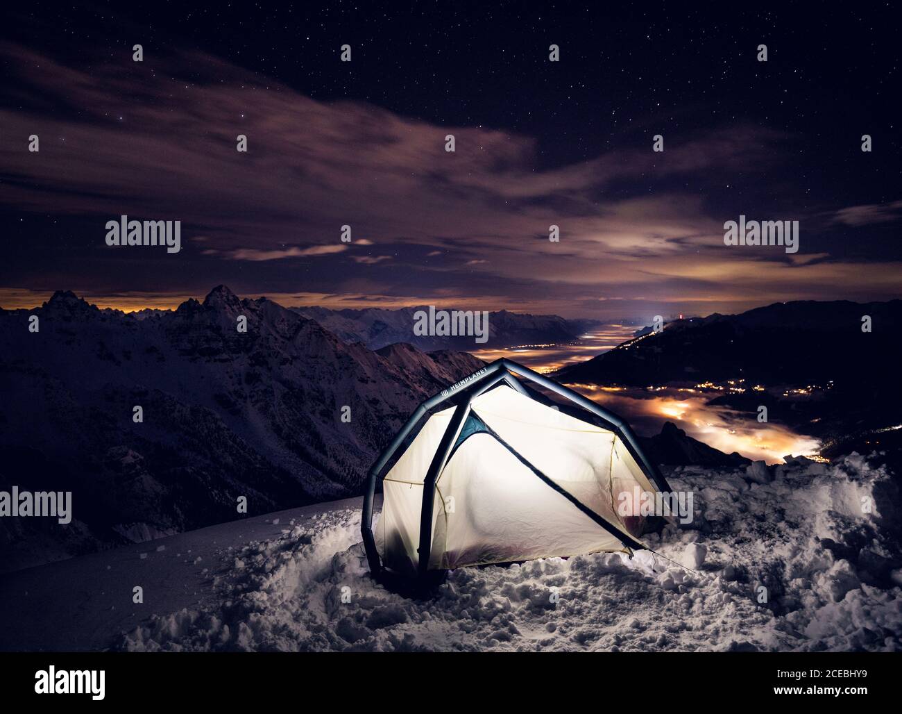 Tenda con luce sulle montagne coperte di neve di notte. Foto Stock