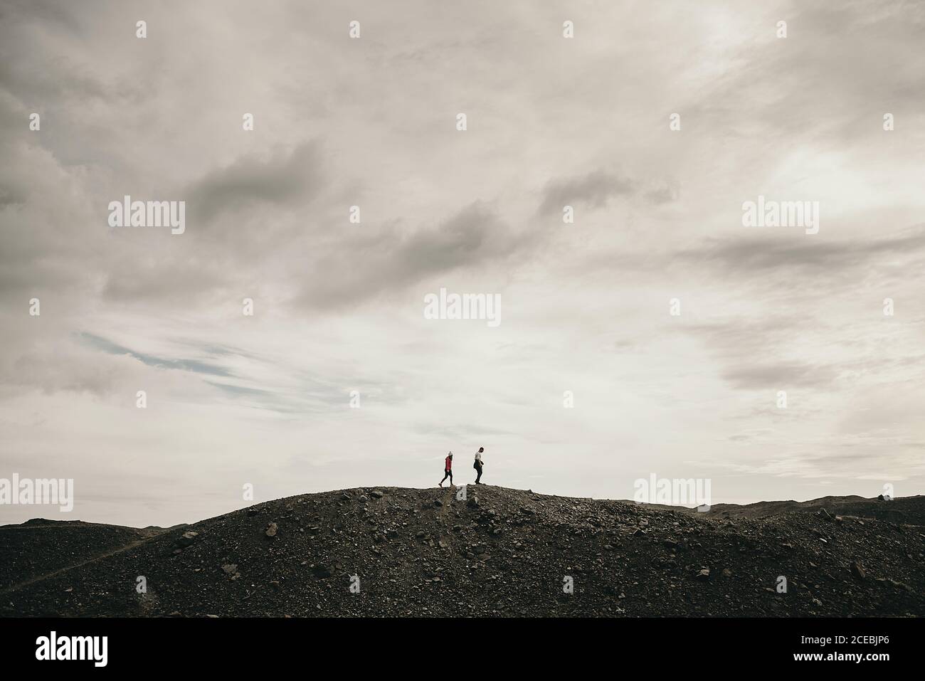 Vista laterale di turisti irriconoscibili che camminano su una collina asciutta in un giorno nuvoloso. Foto Stock
