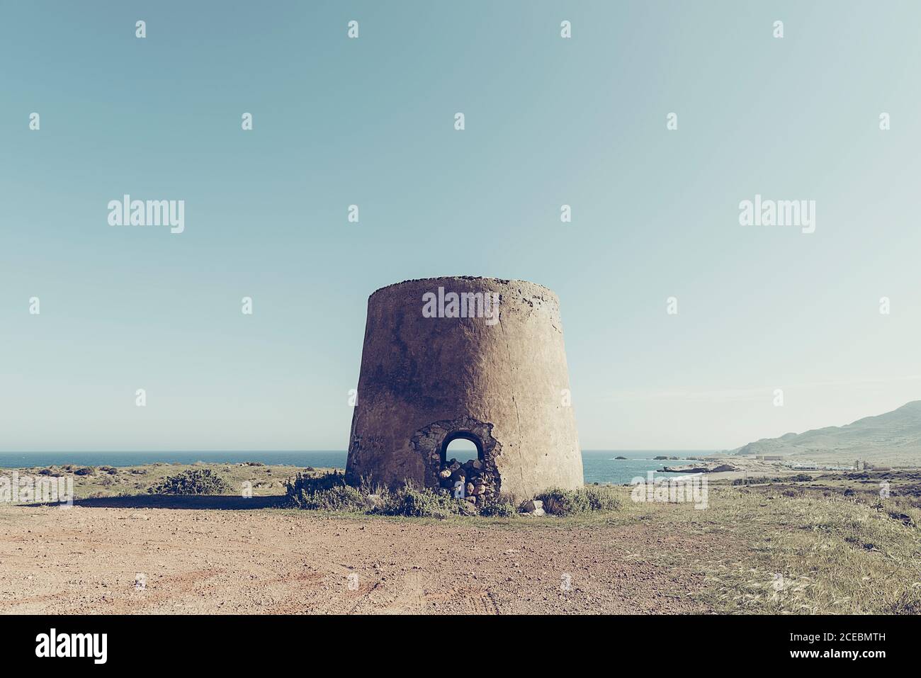 Vecchio terreno rotondo edificio senza tetto su terra sterile a. spiaggia rocciosa dell'oceano in giornata di sole Foto Stock