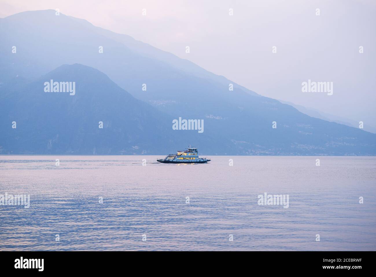 Tramonto e tramonto sul Lago di Como. Italia. Lonely Ferry galleggia su una tranquilla superficie d'acqua. Vista idilliaca. Foto Stock