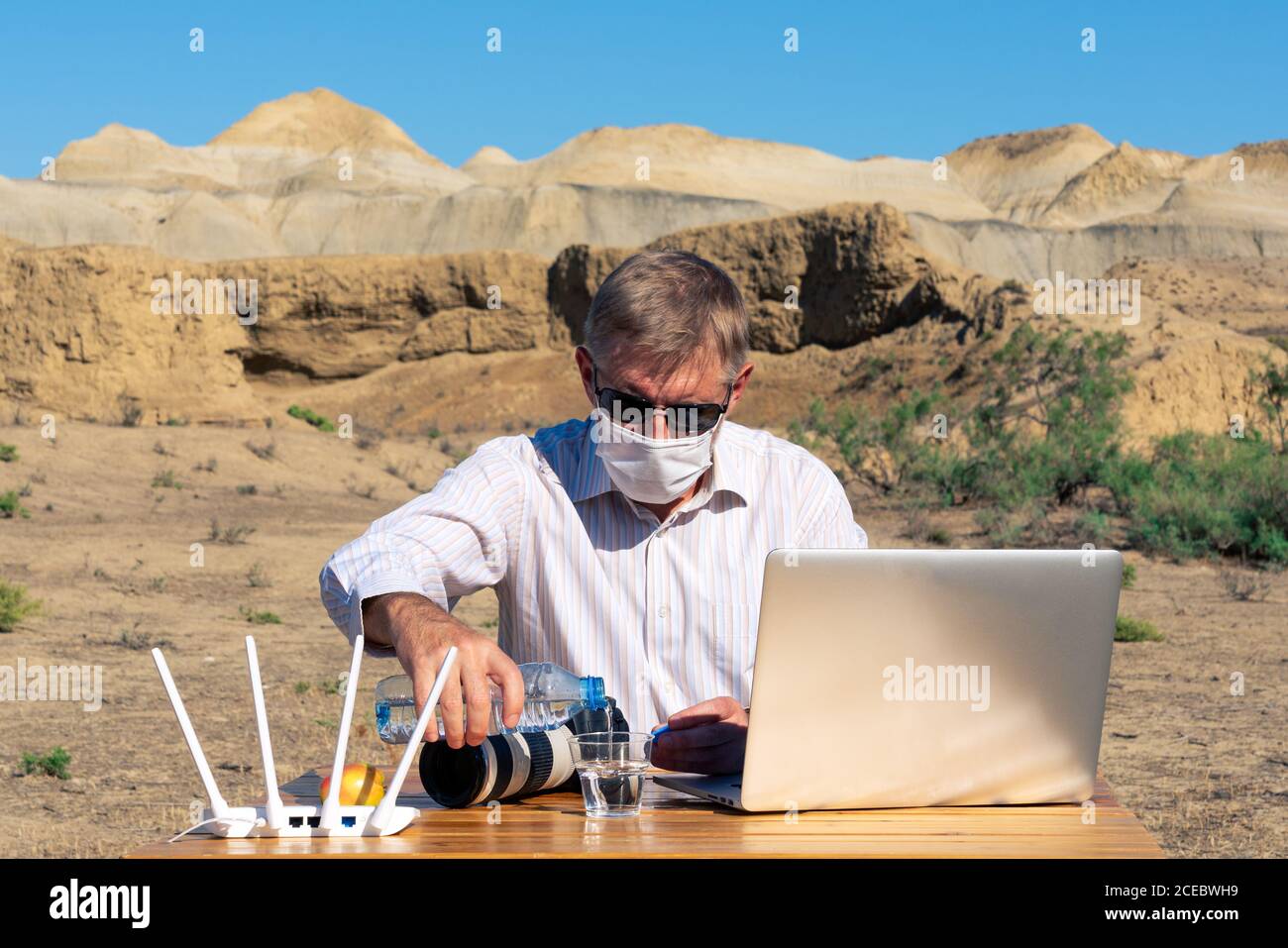 Fotografo in maschera medica lavora all'aperto su un computer portatile Foto Stock