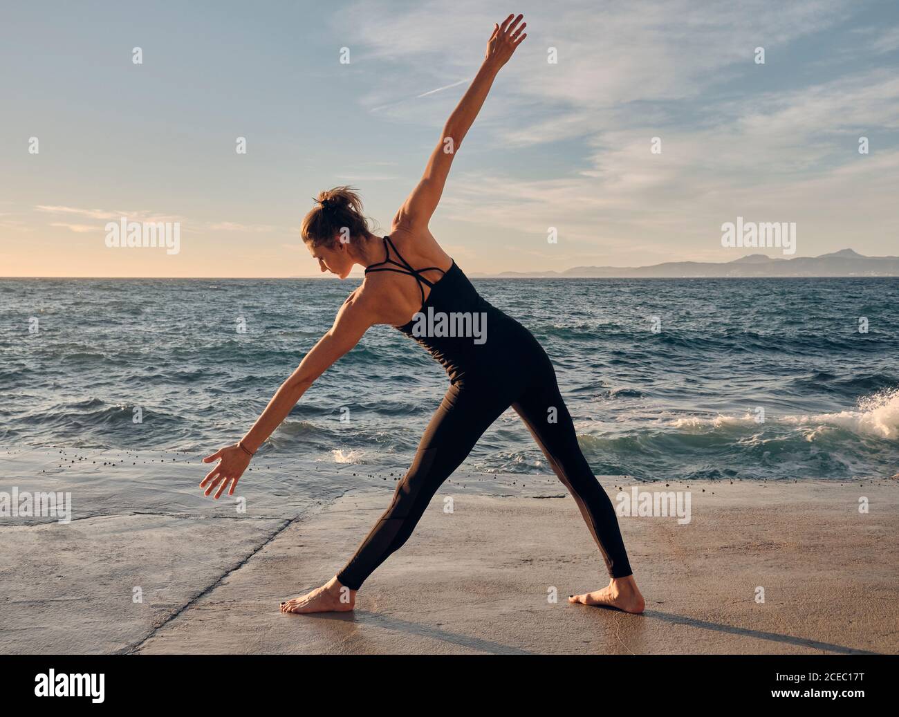 Giovane donna in piedi in Triangolo posa vicino al mare Foto Stock