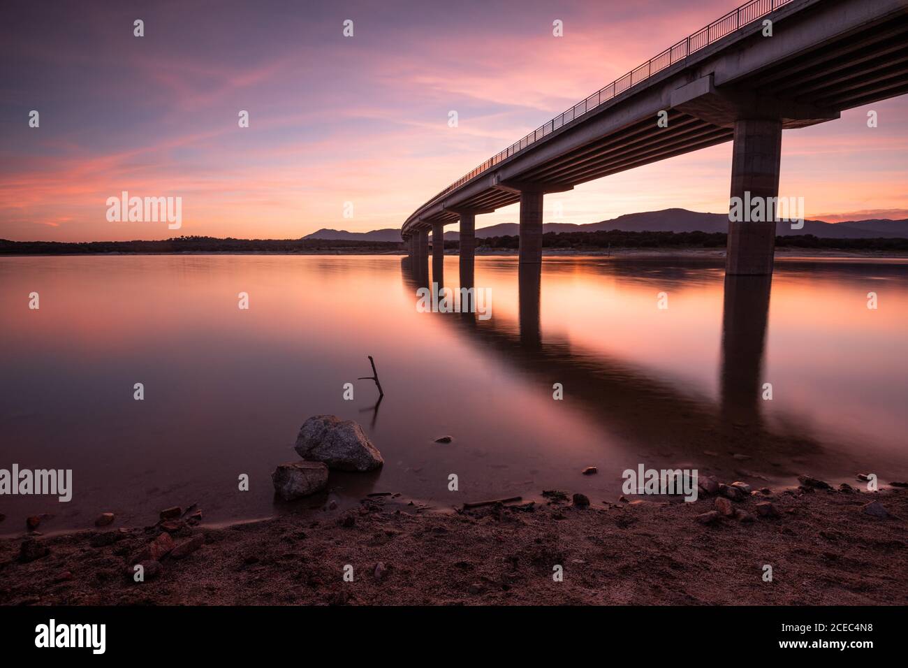 Lungo ponte e acque calme dell'incredibile bacino idrico di Valmayor durante magnifico tramonto Foto Stock