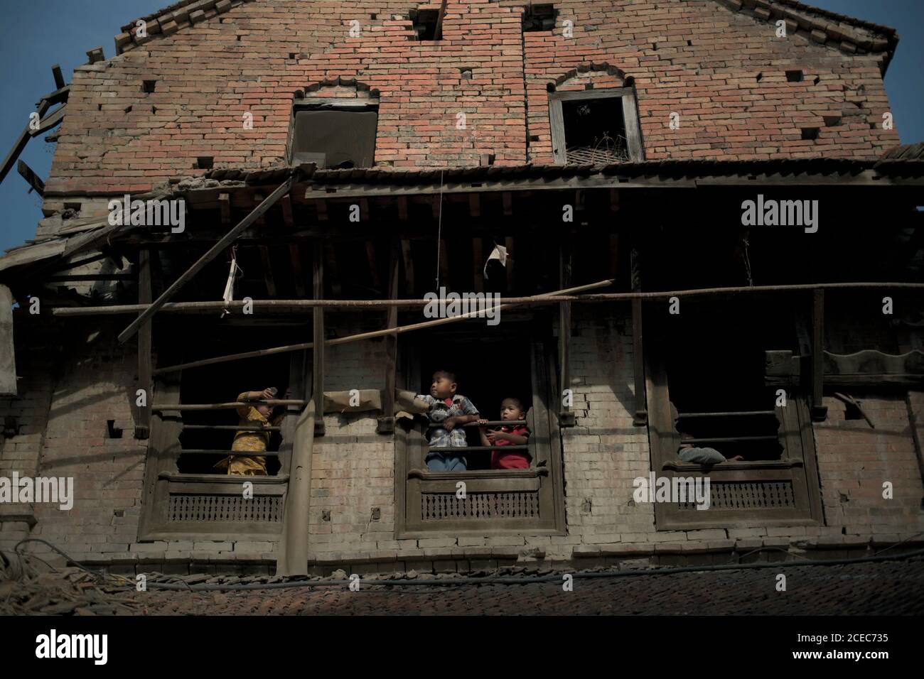 Bambini che giocano alle finestre di una casa gravemente danneggiata dai terremoti del 2015 Nepal a Bhaktapur, Bagmati Pradesh, Nepal. Foto Stock