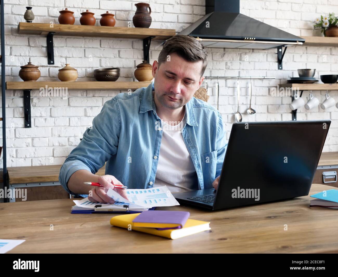 Un uomo lavora a casa con documenti e un computer portatile. Lavoro remoto. Foto Stock