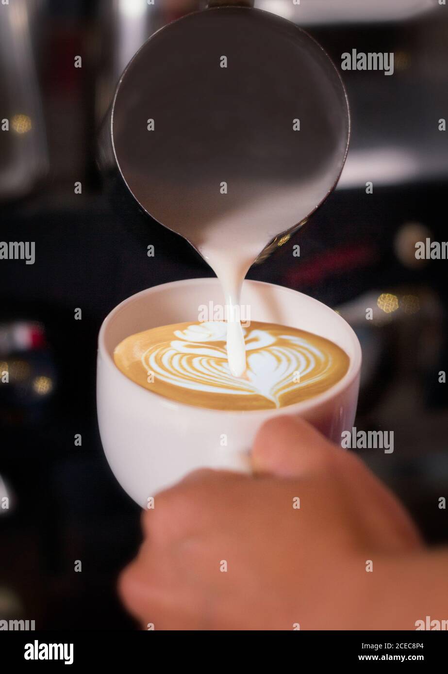Crop mano di irriconoscibile barman versando crema al latte e disegnare un fiore. Foto Stock
