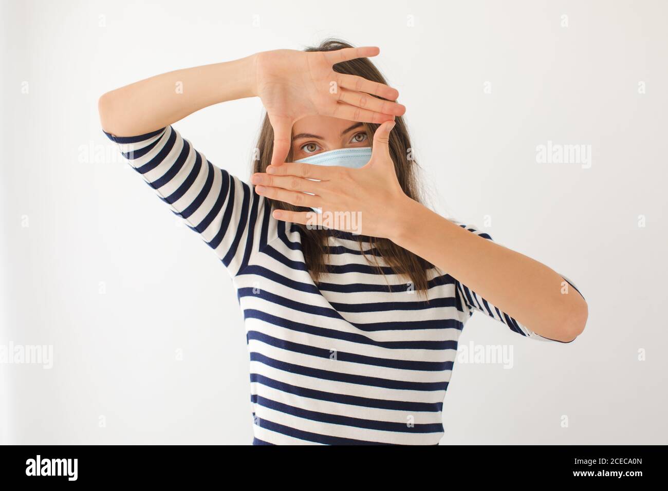 Giovane donna in maschera medica che fa cornice con le mani Foto Stock