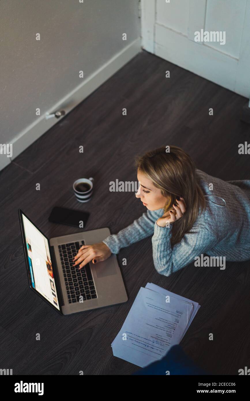 Donna sdraiata sul pavimento che lavora con un computer portatile Foto Stock