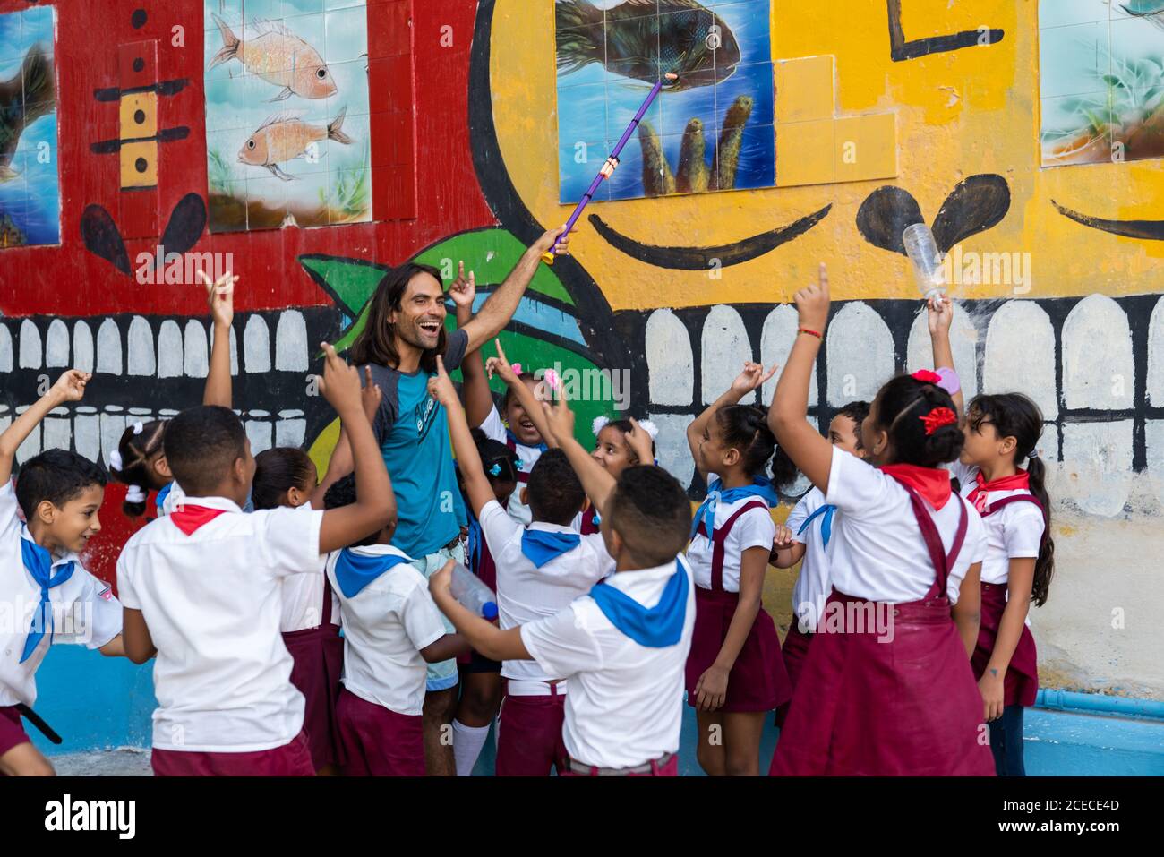 LA HABANA, CUBA - NOVEMBRE, 6 , 2018: Giovane uomo sorridente con puntatore che mostra sulla foto del pesce tra le uniformi pioniere afro-americane dei bambini?in che si sollevano le mani vicino al muro a Cuba Foto Stock