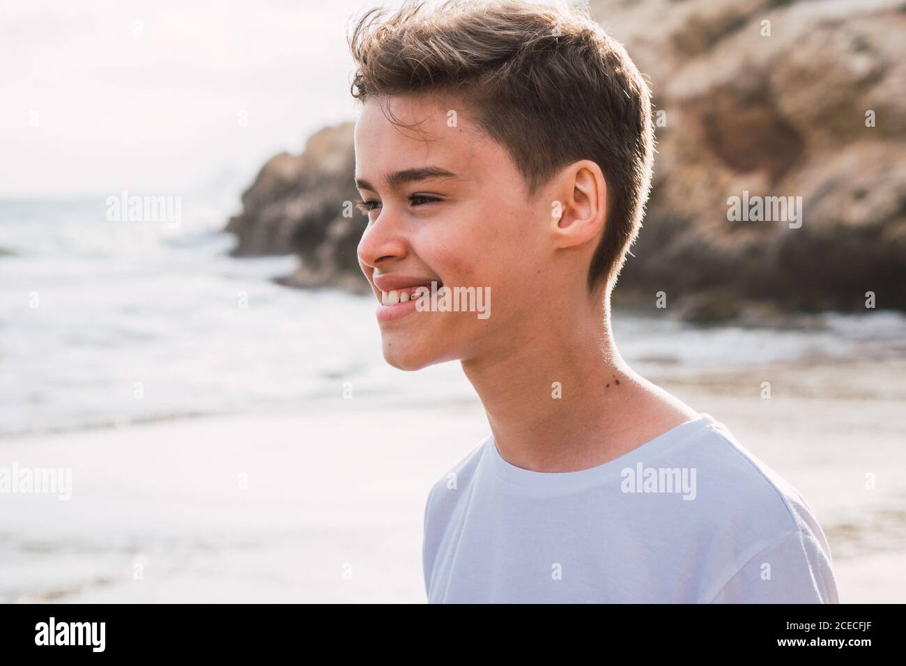 sorridente ragazzo carino in t-shirt bianca che cammina sul mare a. estate Foto Stock