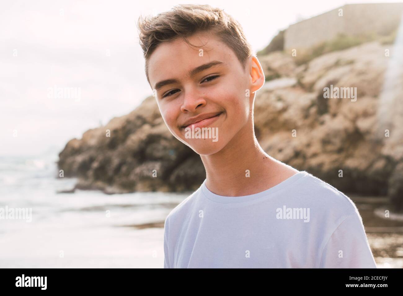 sorridente ragazzo carino in t-shirt bianca che cammina sul mare a. estate Foto Stock