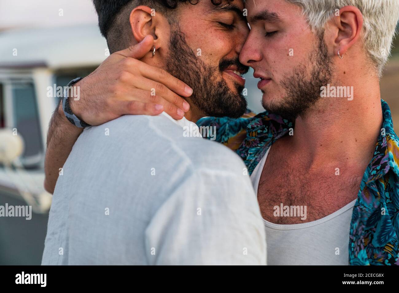 Vista laterale di bei giovani che abbracciano e baciano mentre in campagna vicino a un furgone retrò Foto Stock