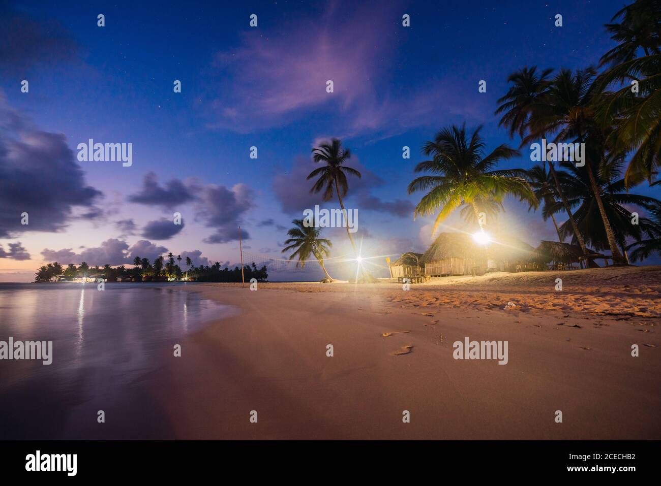 Spiaggia di sabbia con alberi tropicali e la costruzione con lampade illuminate vicino al mare e cielo blu in serata a San Blas isole, Panama Foto Stock