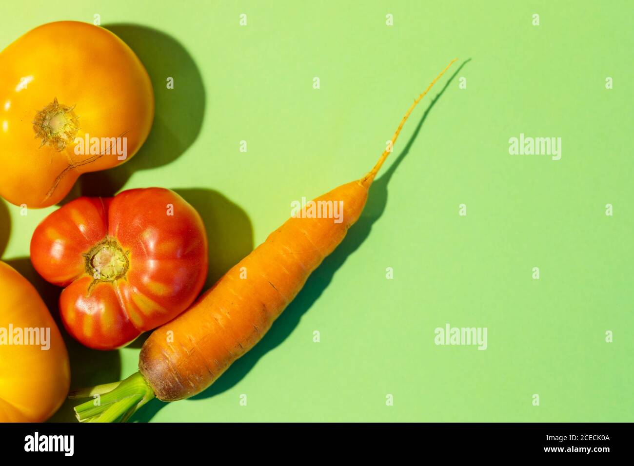 Vista sopra verdure succose mature - pomodori e carote su sfondo verde con spazio copia. Pubblicità autunno raccolto sfondo. Foto Stock