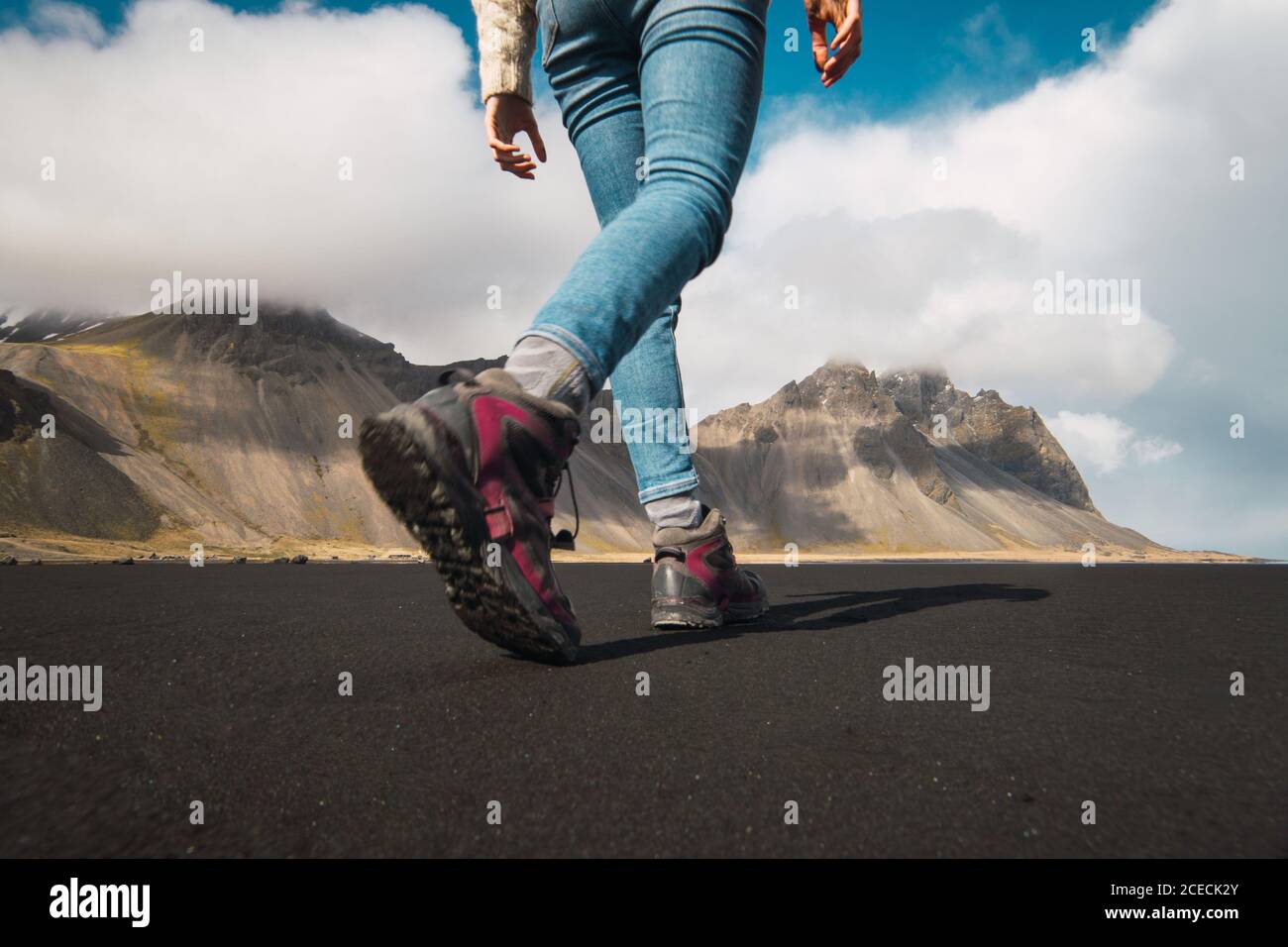 Foto senza volto dal basso di Donna in scarpe da trekking a piedi sul terreno della valle con montagne sullo sfondo, Islanda. Foto Stock