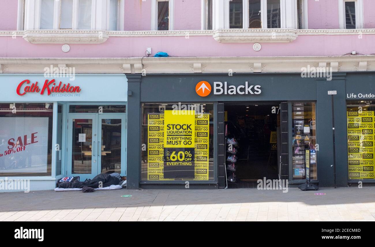 Uomo senza casa che dorme nella porta del negozio chiuso Cath Kidston Accanto al negozio all'aperto Blacks, che ha un magazzino Vendita di liquidazione in North Street Brighton Foto Stock