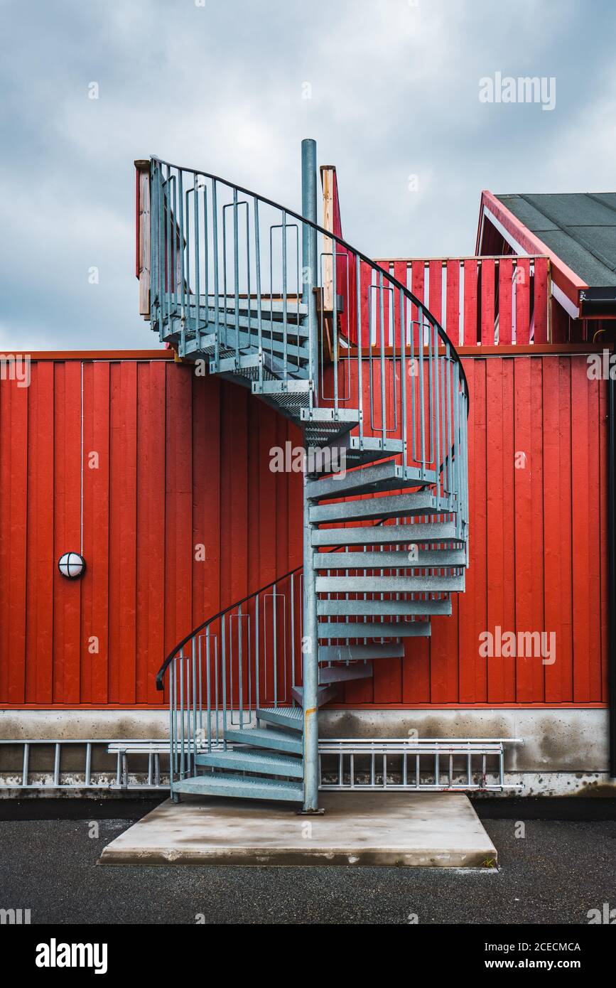 Scala in metallo avvolgente che conduce alla casa posta dietro l'alto rosso recinzione sullo sfondo del cielo nuvoloso Foto Stock