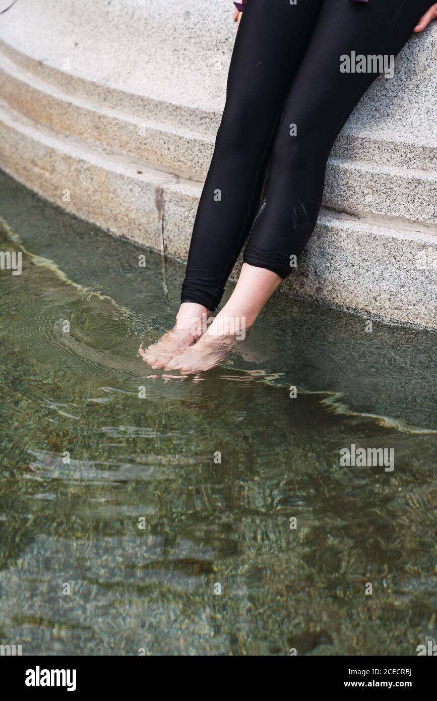 Raccolto dall'alto di Woman gambe in collant nero messo in trasparente acqua calma Foto Stock