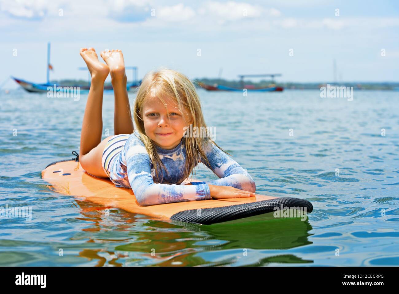 Happy baby girl - giovane surfista imparare a cavalcare sulla tavola da surf con divertimento sulle onde del mare. Stile di vita familiare attivo, lezioni di sport acquatici all'aperto per bambini, nuoto Foto Stock