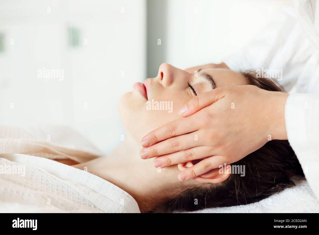 MMasseuse in abito in piedi nel salone termale e massaggiante viso di cliente femminile Foto Stock