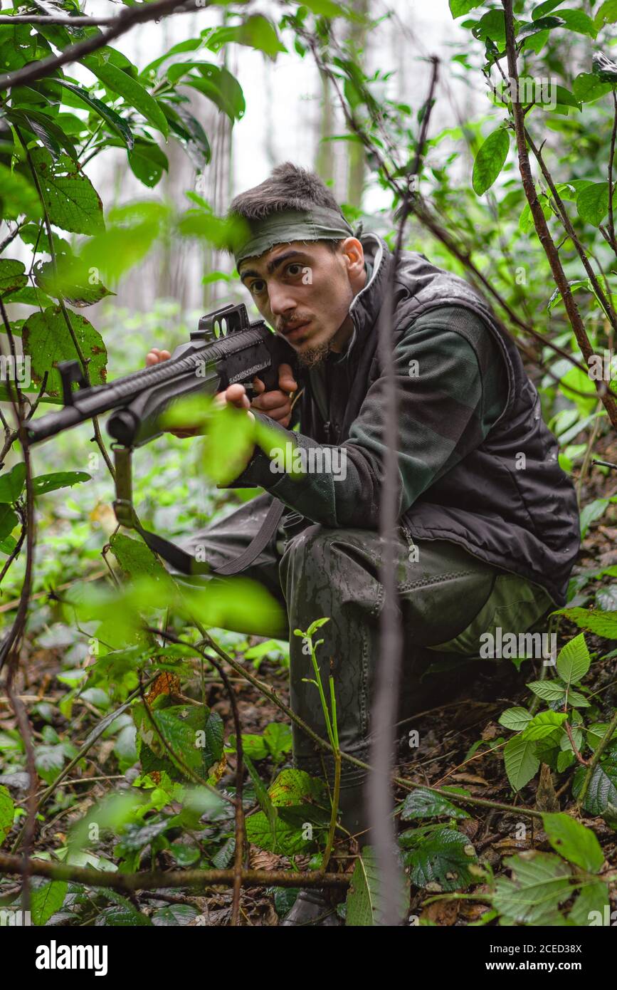 Soldato o membro rivoluzionario o cacciatore che mira con la pistola in mano in camuffamento nella foresta, concetto di caccia Foto Stock